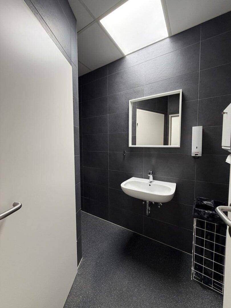Modernes WC mit dunkelgrauen Fliesen, weißem Waschbecken und einem Spiegel.