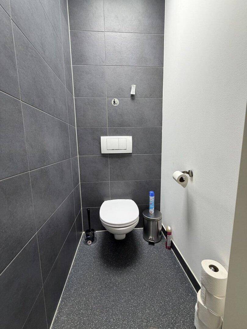Modernes WC mit dunkelgrauen Fliesen und einer wandhängenden Toilette.