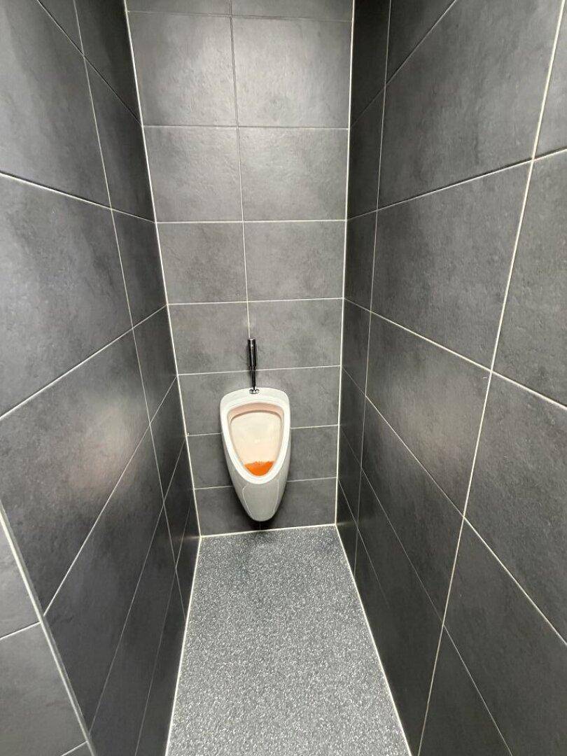 Modernes WC mit dunkelgrauen Fliesen und einem Urinal.