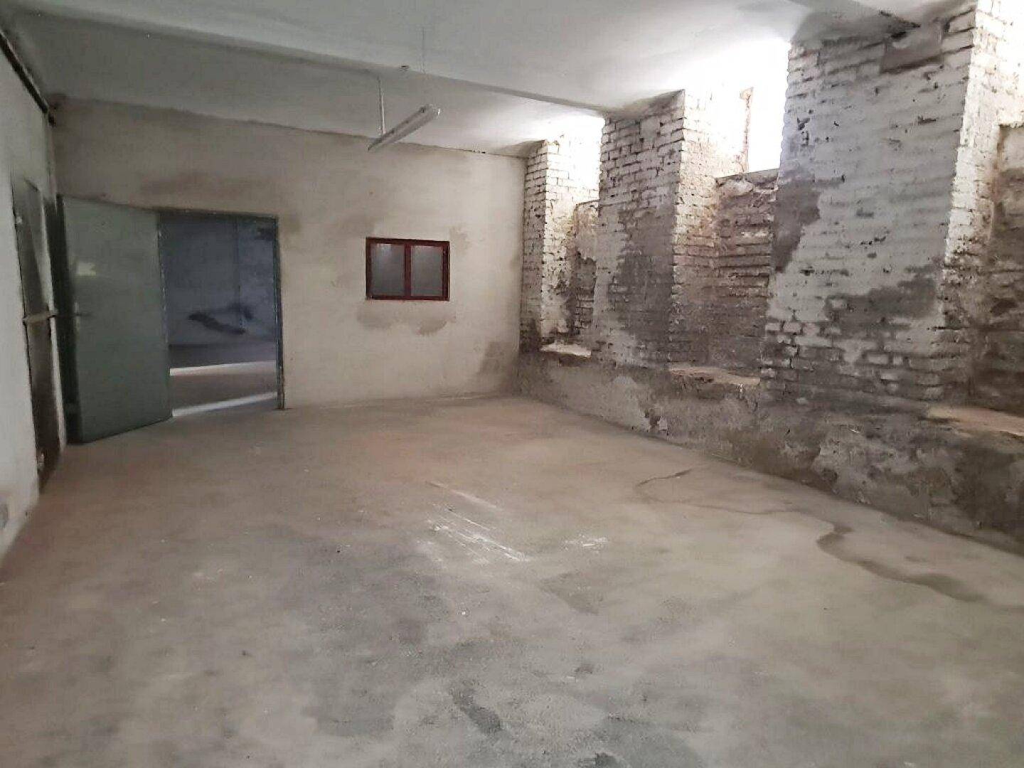 Geräumiger Kellerraum mit Betonboden, unverputzten Ziegelwänden und einem kleinen Fenster, ideal als Lagerfläche.