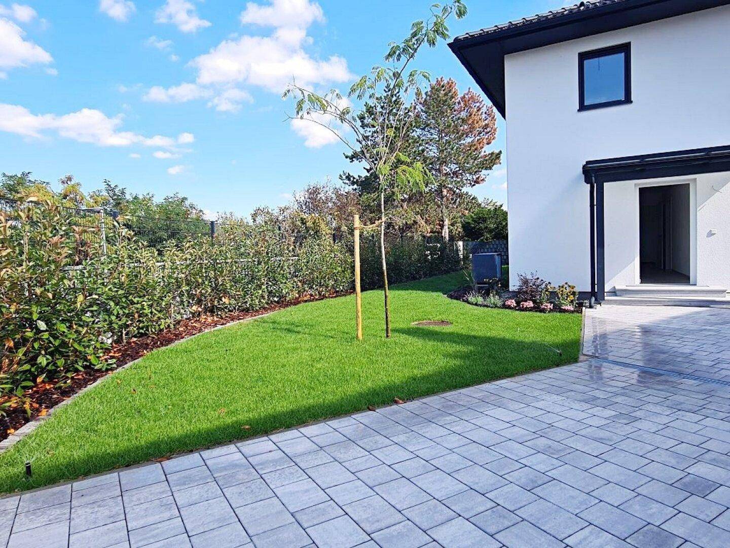 Gepflegter Gartenbereich mit Rasenfläche und gepflastertem Zugang zum Haus.