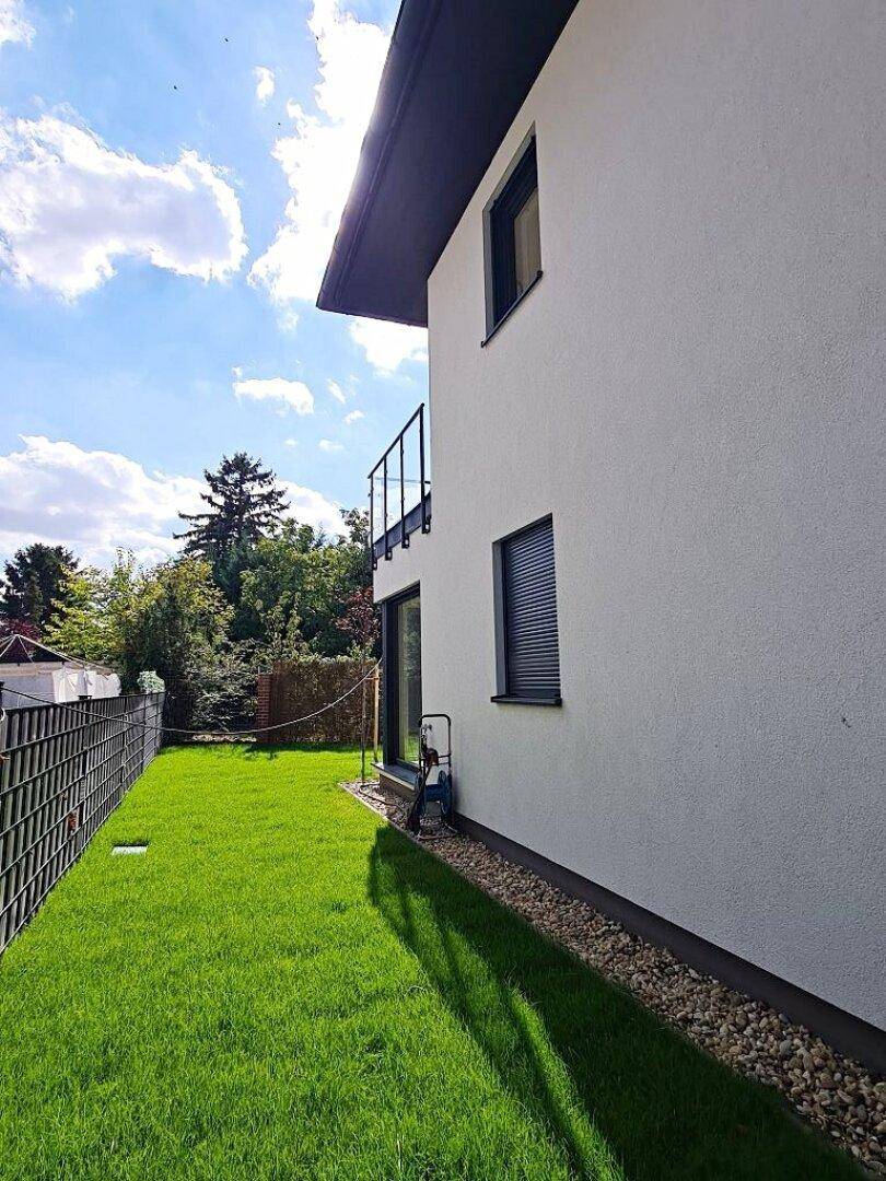 Seitenansicht des Hauses mit grünem Rasen, kleinem Balkon und moderner Fassade.