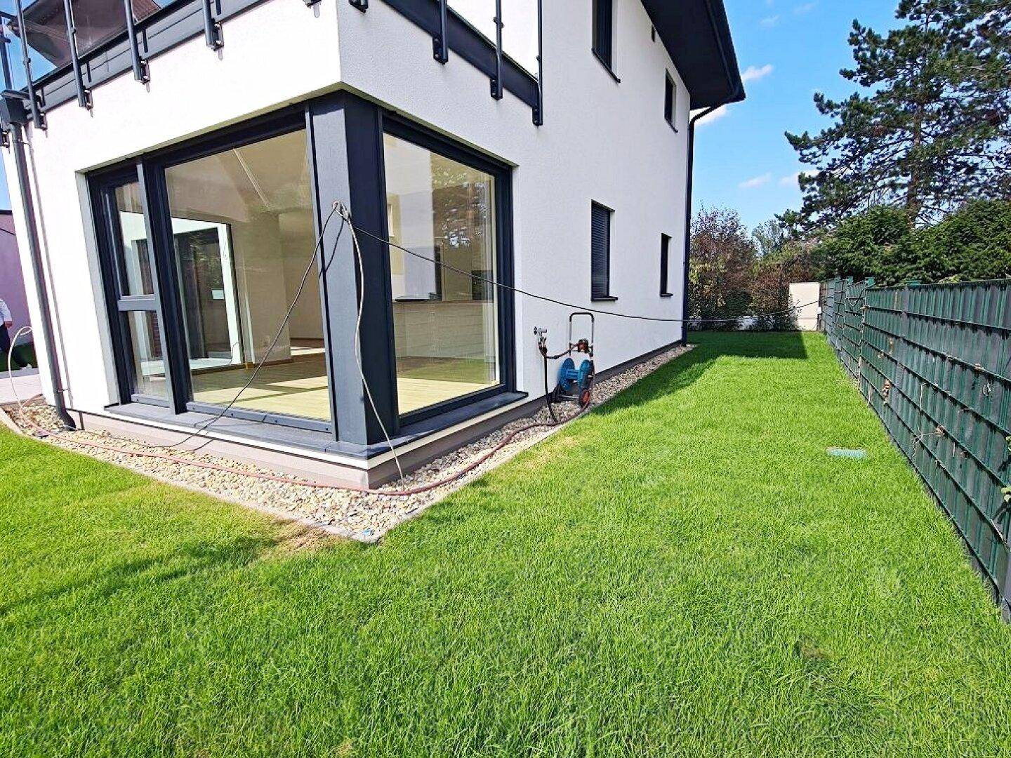 Seitlicher Gartenbereich mit Rasen, Kiesstreifen und Blick auf die Hausfassade.