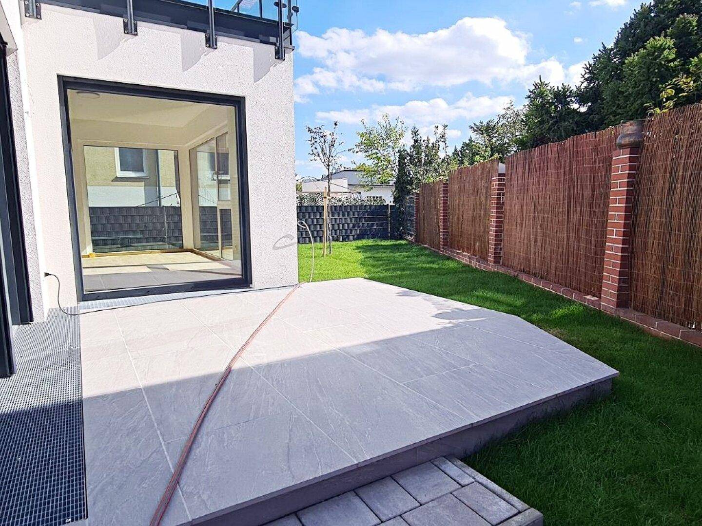 Sonniger Terrassenbereich mit Fliesenboden und angrenzendem Garten mit Zaun.