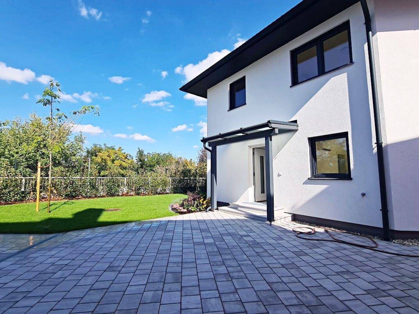 Rückseite des Hauses mit gepflastertem Bereich, Rasenfläche und Blick in den Garten.