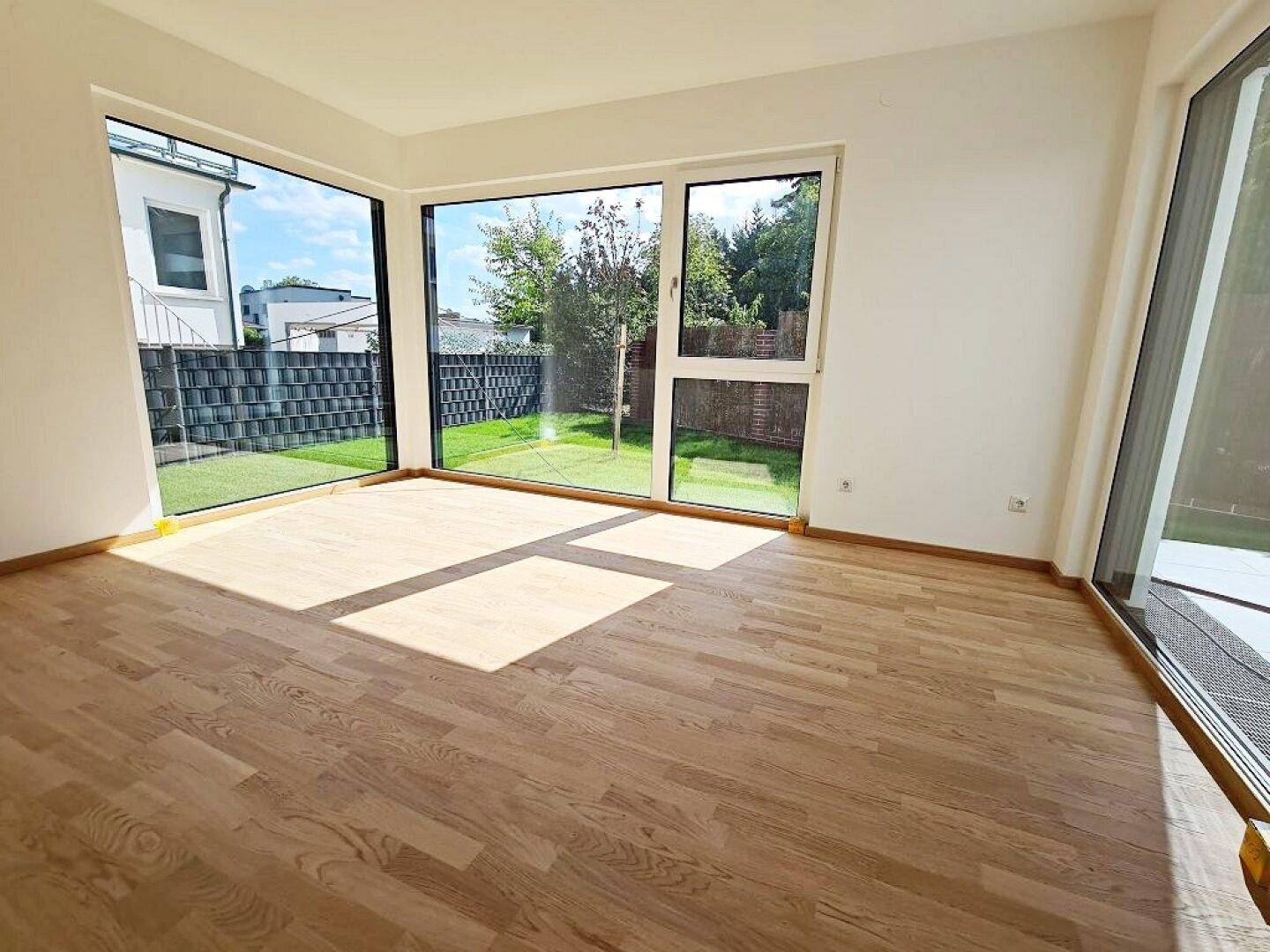 Heller Wohnraum mit großen Fenstern, Holzboden und viel Tageslicht.