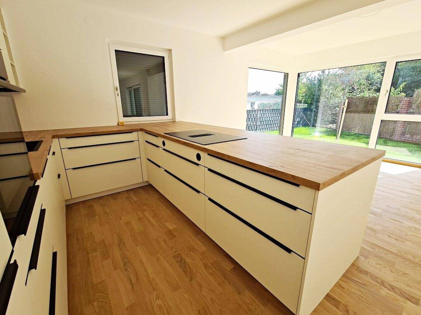 Helle Küche mit Kochinsel, Holz-Arbeitsplatte und Blick in den Garten durch das Fenster.