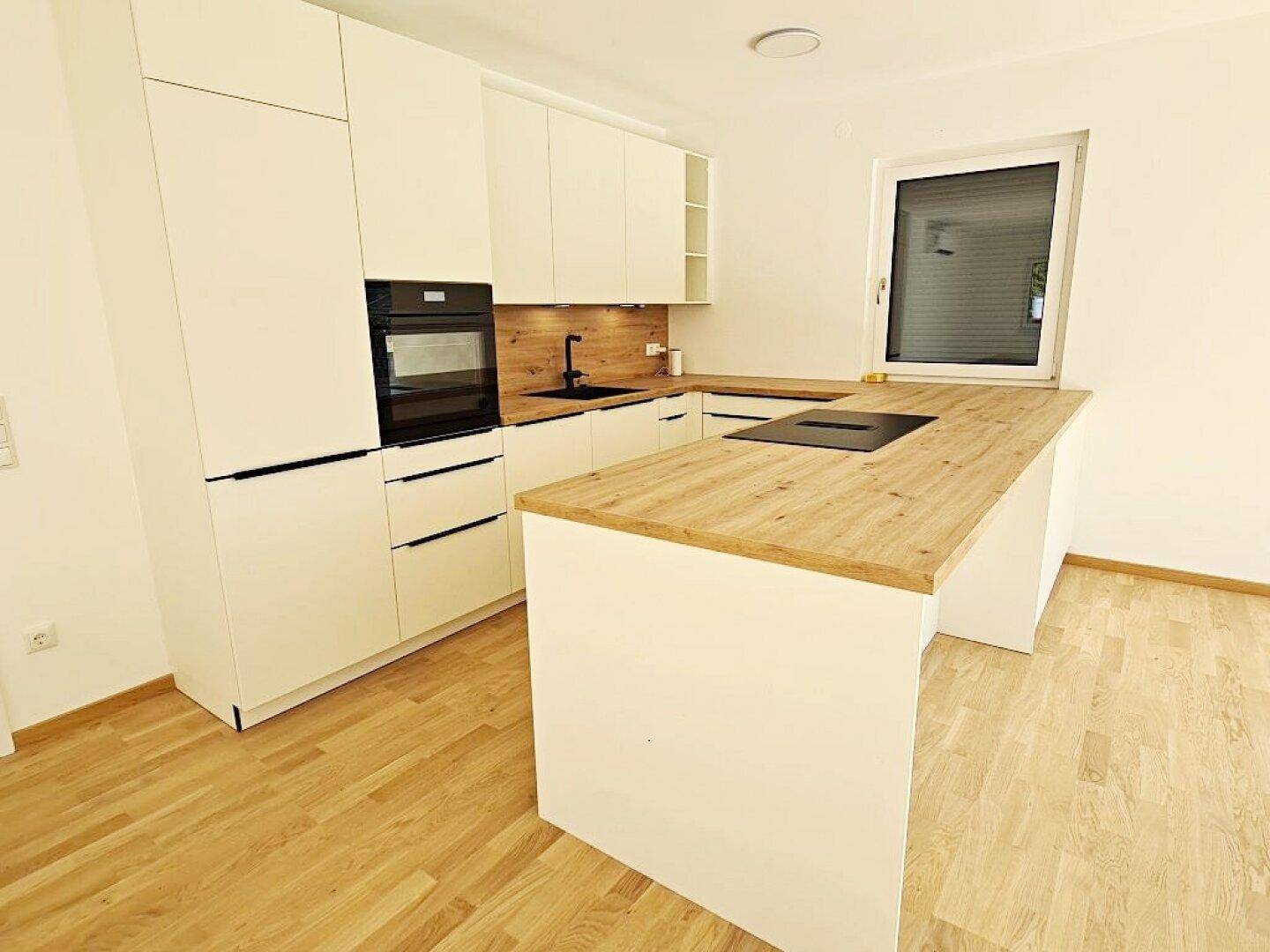 Moderne Einbauküche mit weißer Front, Holz-Arbeitsplatte und Kochinsel.