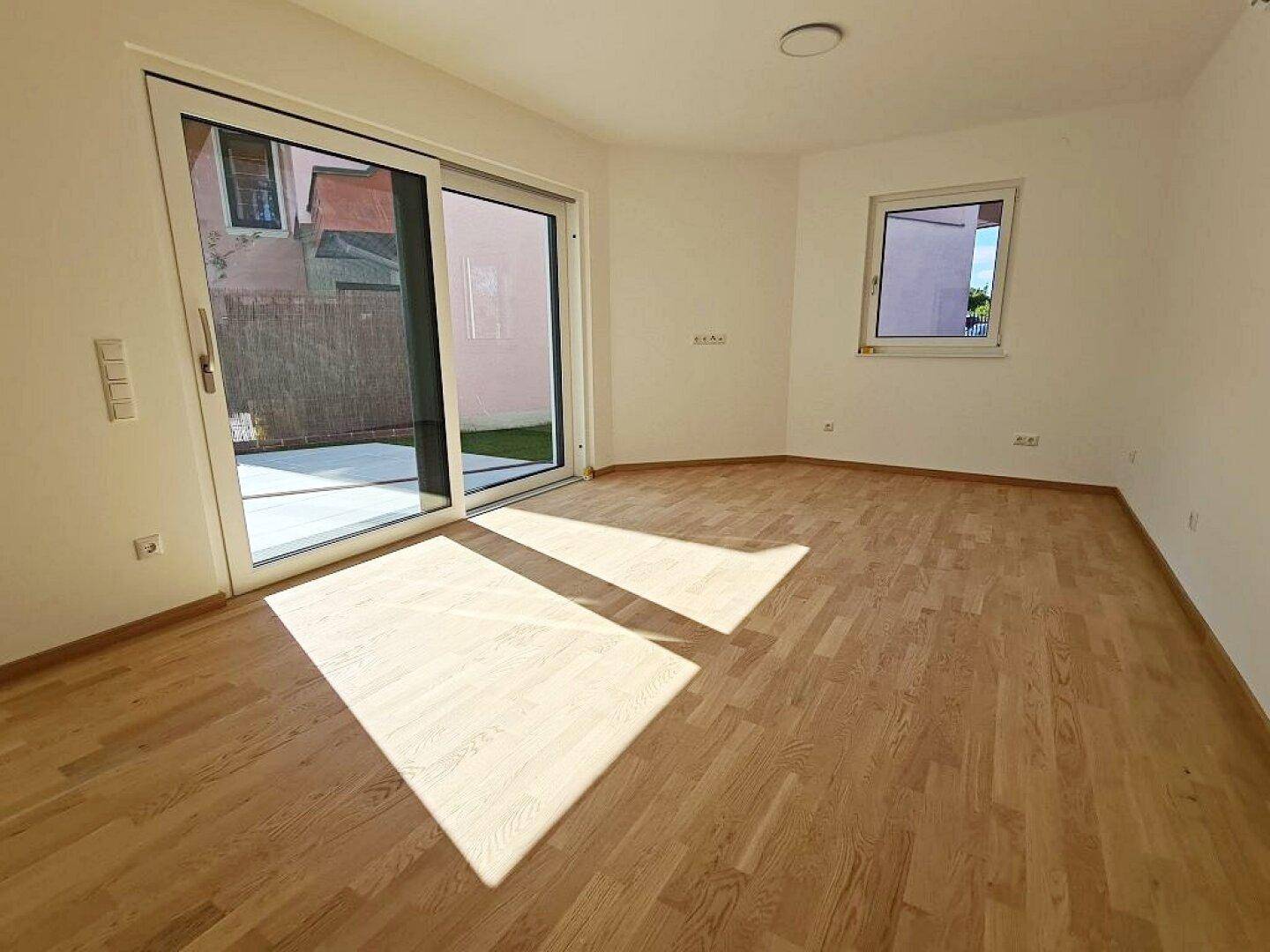 Heller Raum mit Holzboden und großer Schiebetür zum Außenbereich.