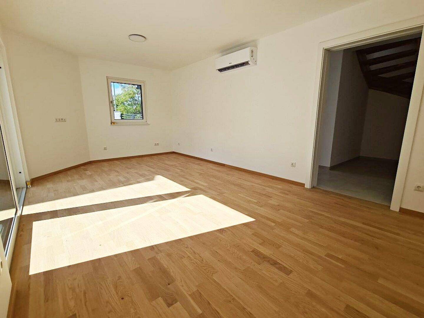 Geräumiges Schlafzimmer mit Holzboden, Fenster und Klimaanlage.