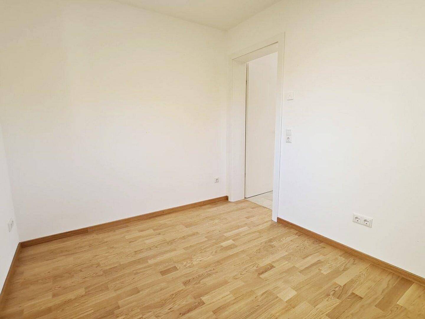 Leeres Zimmer mit Parkettboden und weiß gestrichenen Wänden, bereit zur individuellen Gestaltung.