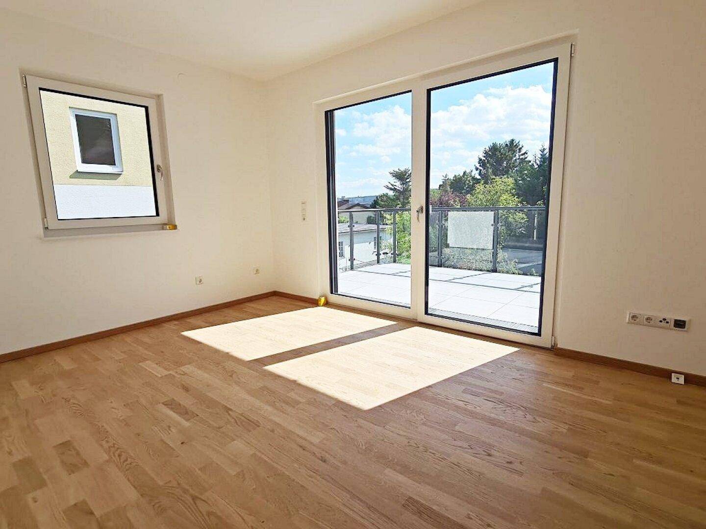 Sonniges Zimmer mit Zugang zu einer großen Terrasse und hellem Parkettboden.