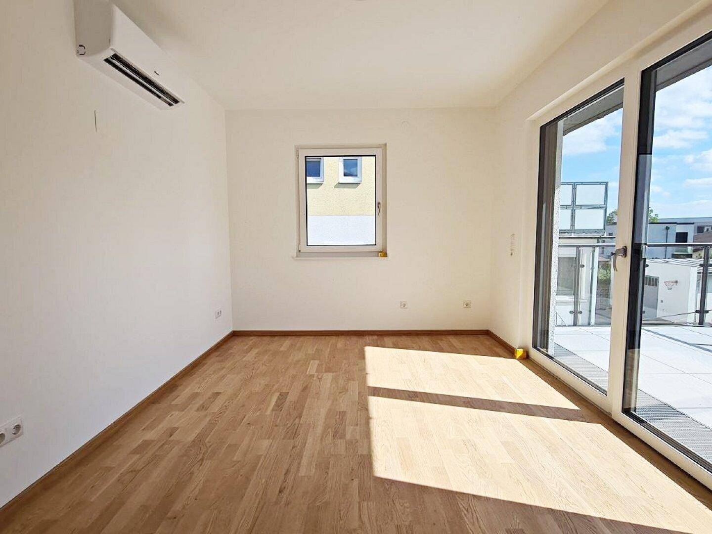 Lichtdurchflutetes Zimmer mit Klimaanlage, Parkettboden und direktem Terrassenzugang.