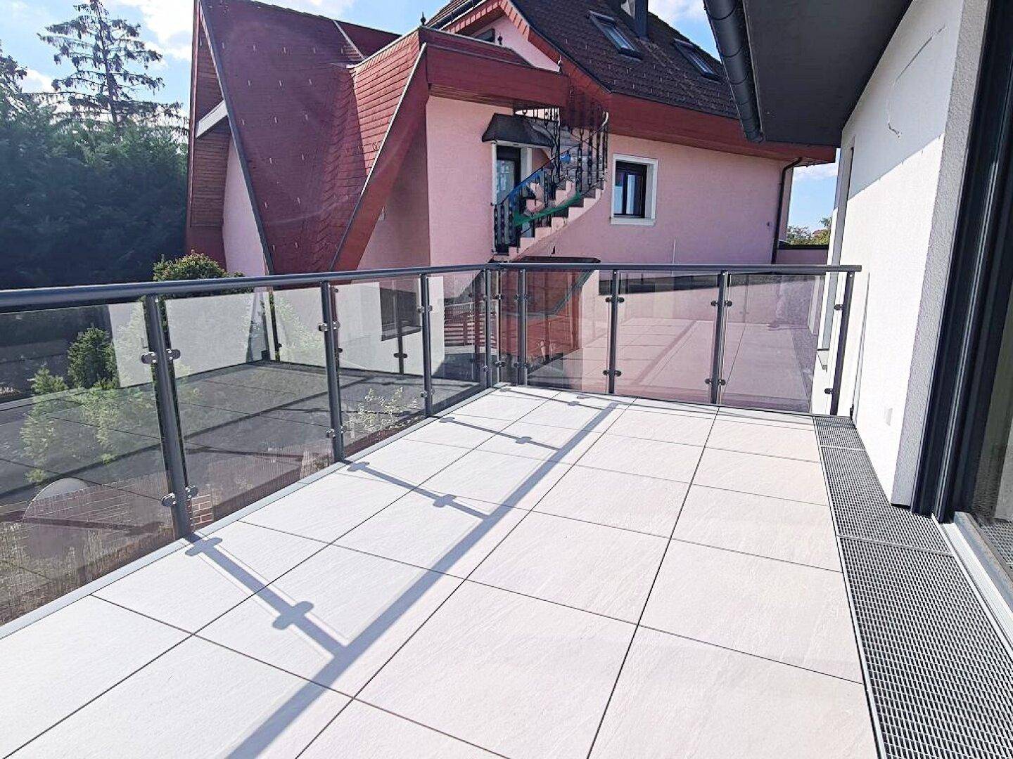 Geräumige, geflieste Terrasse mit Glasgeländer und Blick auf die Umgebung.