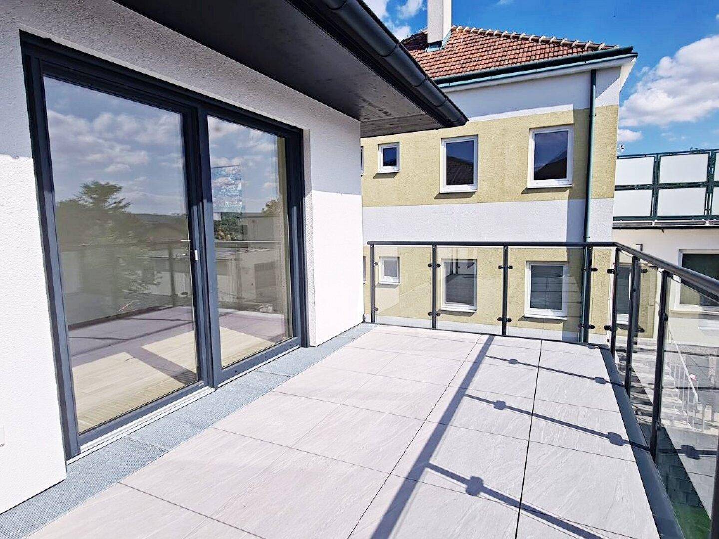 Helle Terrasse mit Fliesenboden und Glasgeländer, bietet einen weiten Blick.