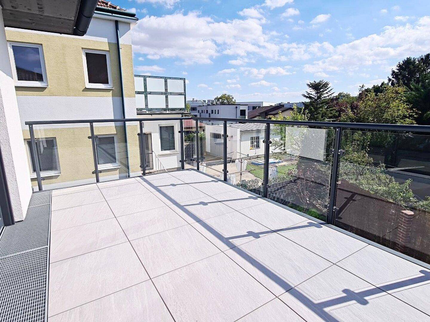 Weitläufige Terrasse mit modernem Glasgeländer und Ausblick auf die Nachbarschaft.