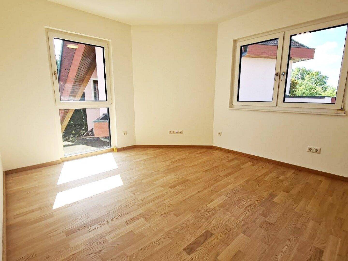 Helles Zimmer mit Parkettboden und zwei Fenstern, bietet viel Tageslicht.