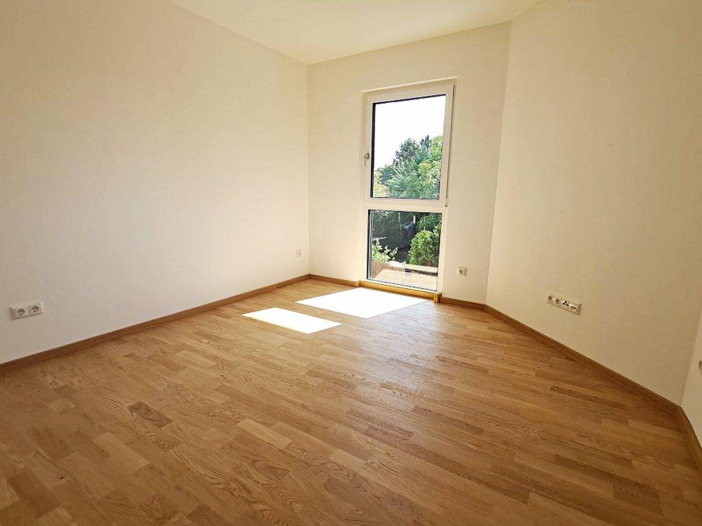 Sonniges Zimmer mit Parkettboden und großem Fenster, bietet eine angenehme Atmosphäre.