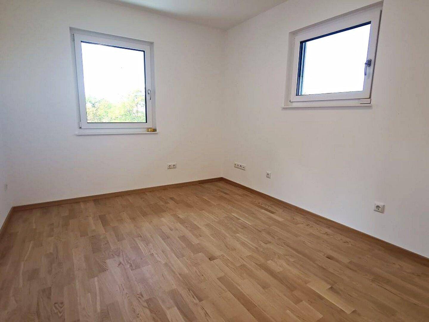 Helles Zimmer mit zwei Fenstern und Parkettboden, bietet viel natürliches Licht.