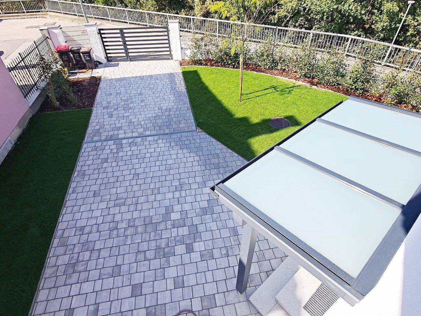 Gepflasterte Einfahrt mit Rasenfläche und Carport, bietet ausreichend Parkmöglichkeiten.