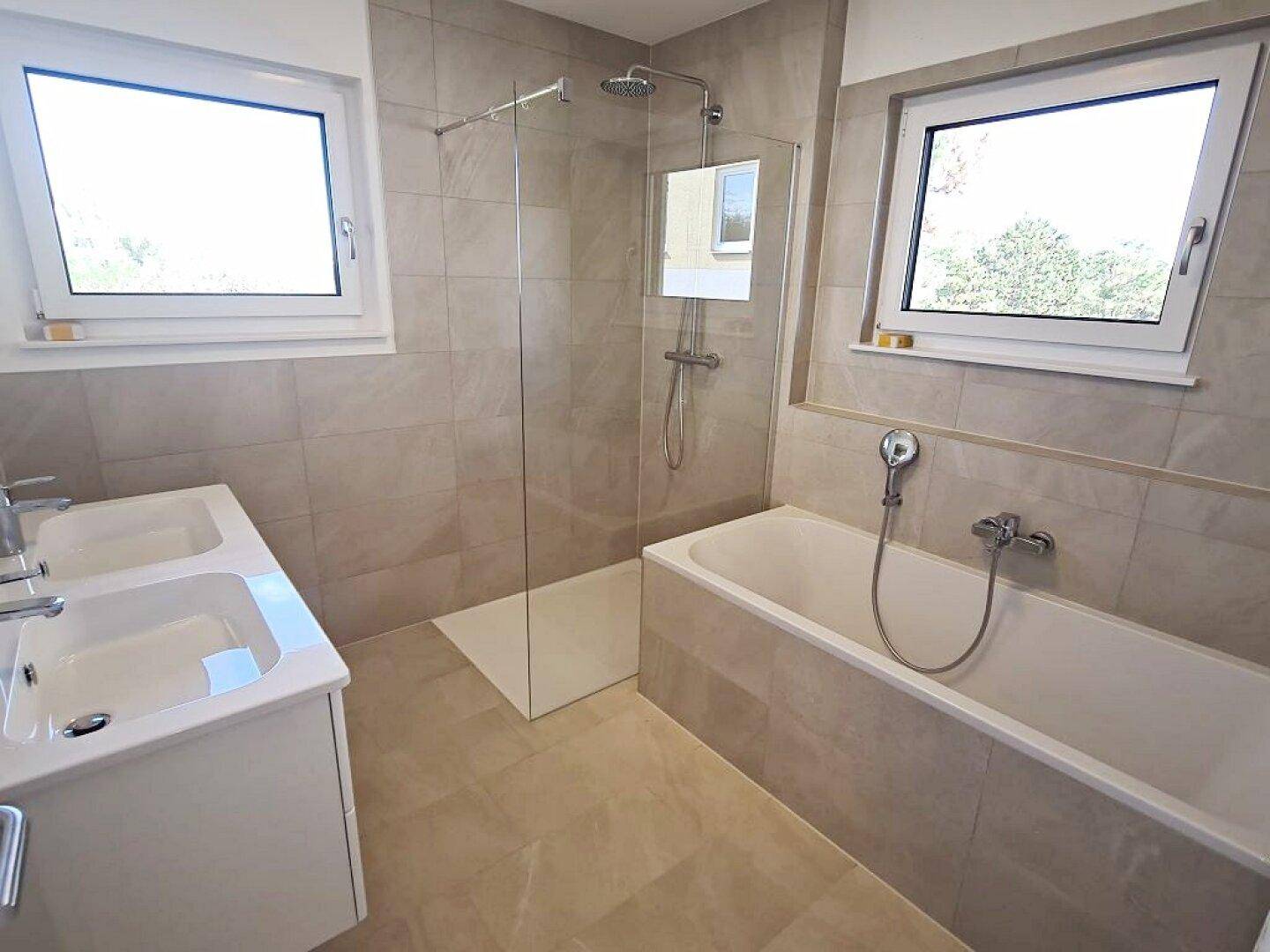 Modernes Badezimmer mit Badewanne, begehbarer Dusche und zwei Fenstern.