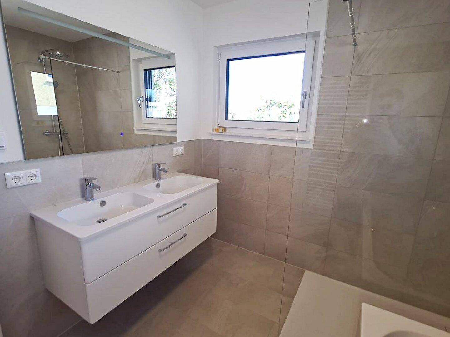 Helles Badezimmer mit Doppelwaschbecken, großem Spiegel und modernen Fliesen.