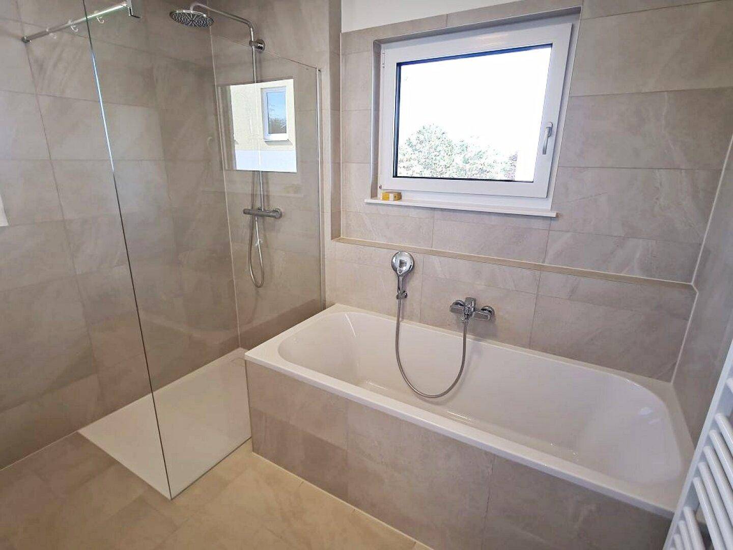 Modernes Badezimmer mit Badewanne und begehbarer Dusche, ausgestattet mit hellen Fliesen.