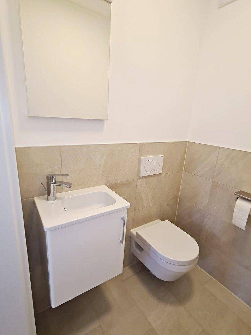Modernes Gäste-WC mit wandhängendem WC, kleinem Waschbecken und Spiegelschrank.