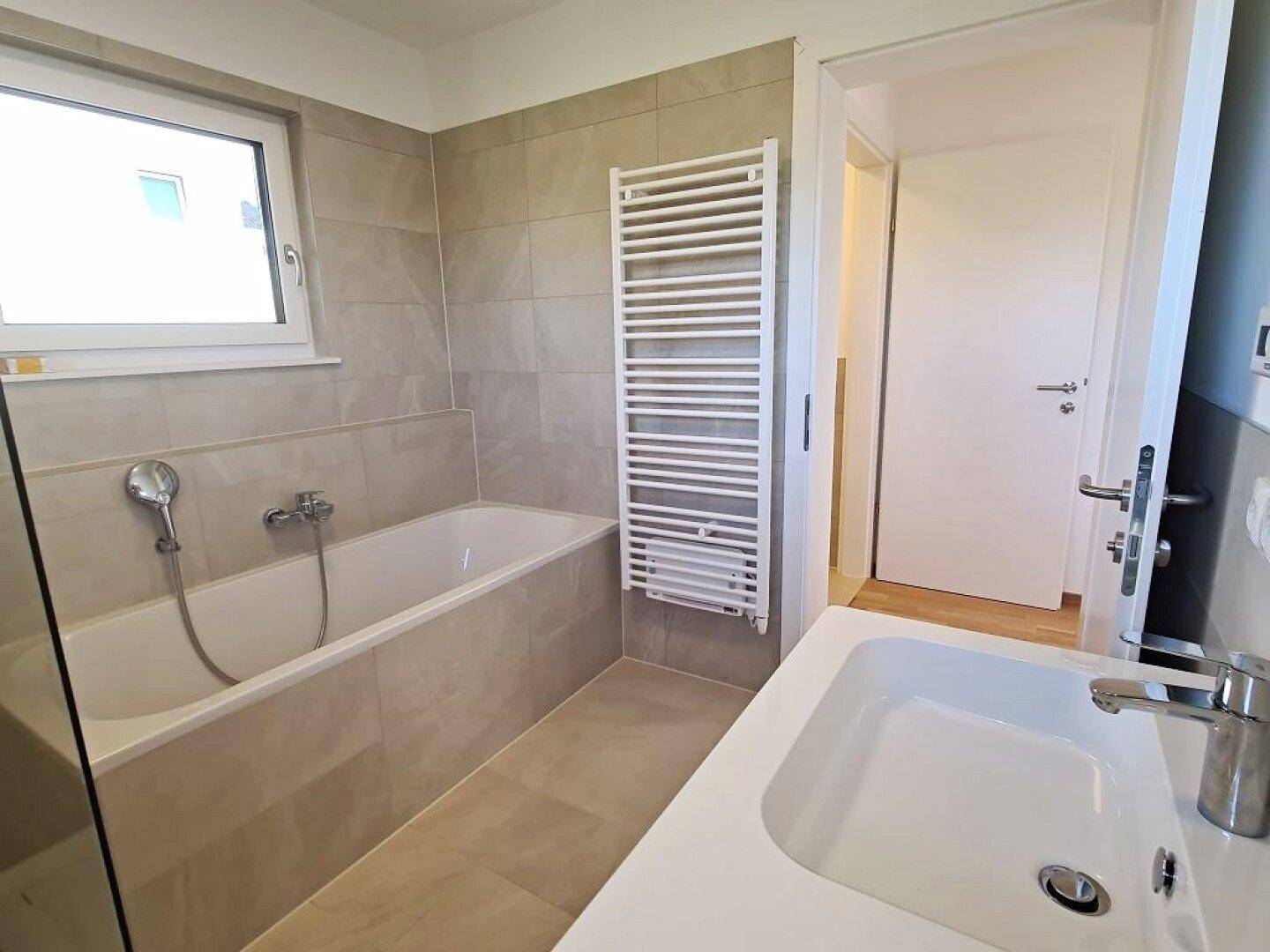Funktionales Badezimmer mit Badewanne, Waschbecken und beheiztem Handtuchhalter.