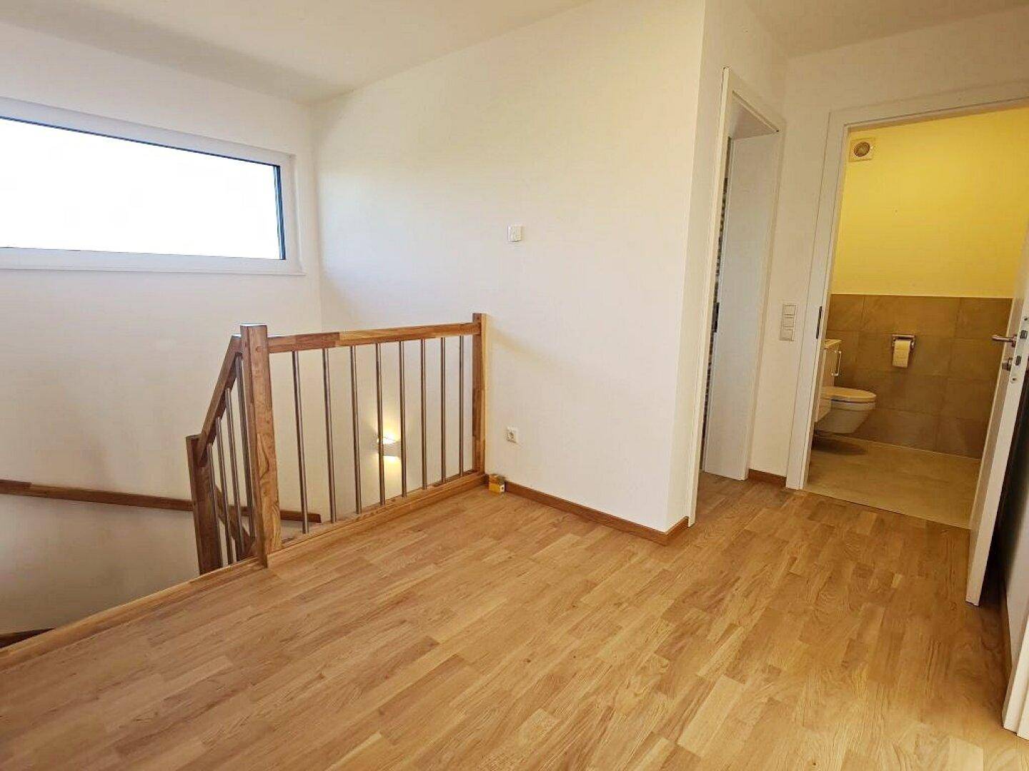 Heller Flur mit Holztreppe und Zugang zu einem Gäste-WC, ausgestattet mit Parkettboden.
