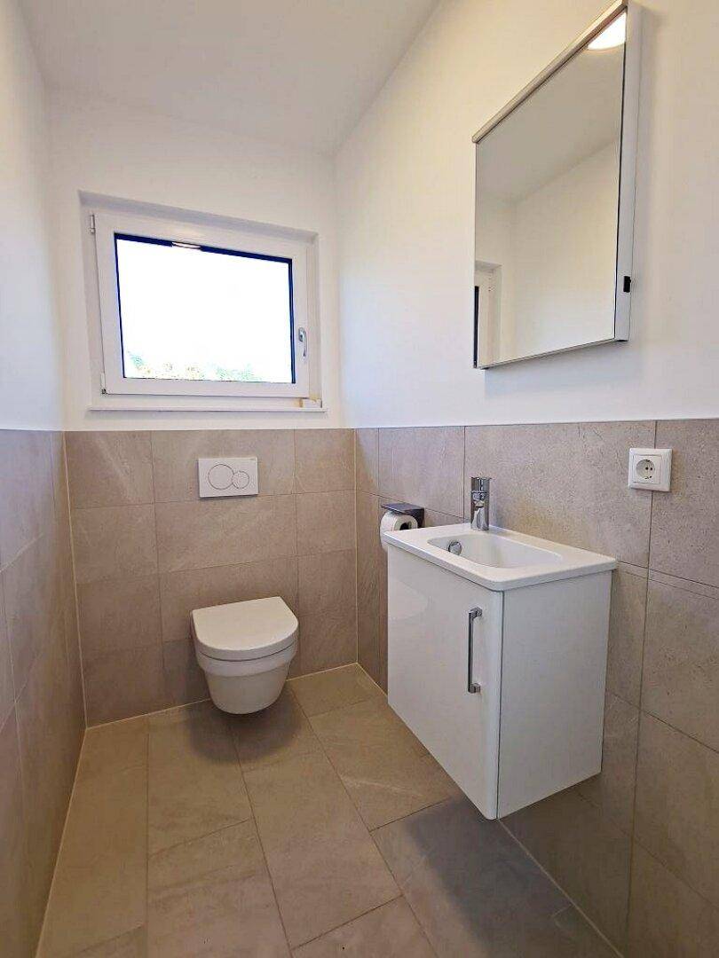 Helles Gäste-WC mit Fenster, wandhängendem WC, Waschbecken und Spiegelschrank.