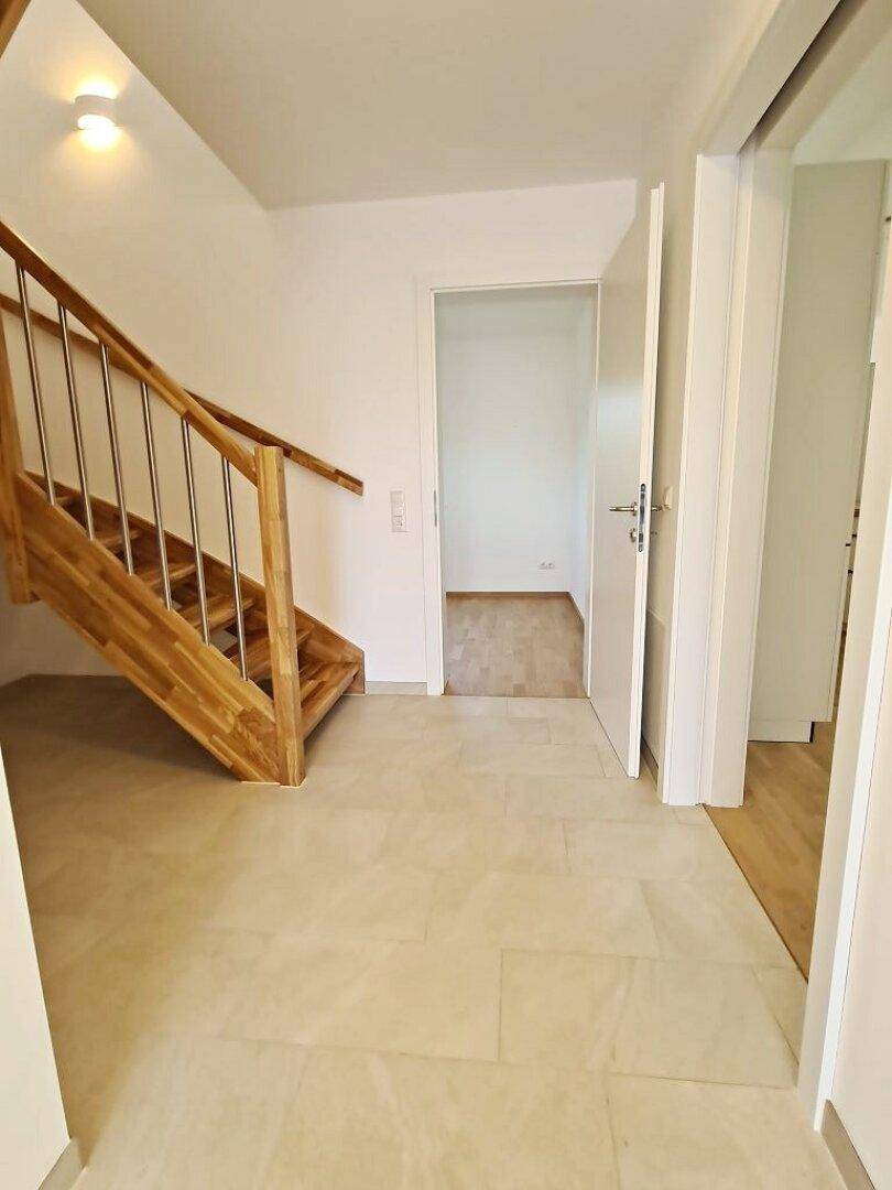 Heller Eingangsbereich mit Fliesenboden und Holztreppe, die ins Obergeschoss führt.