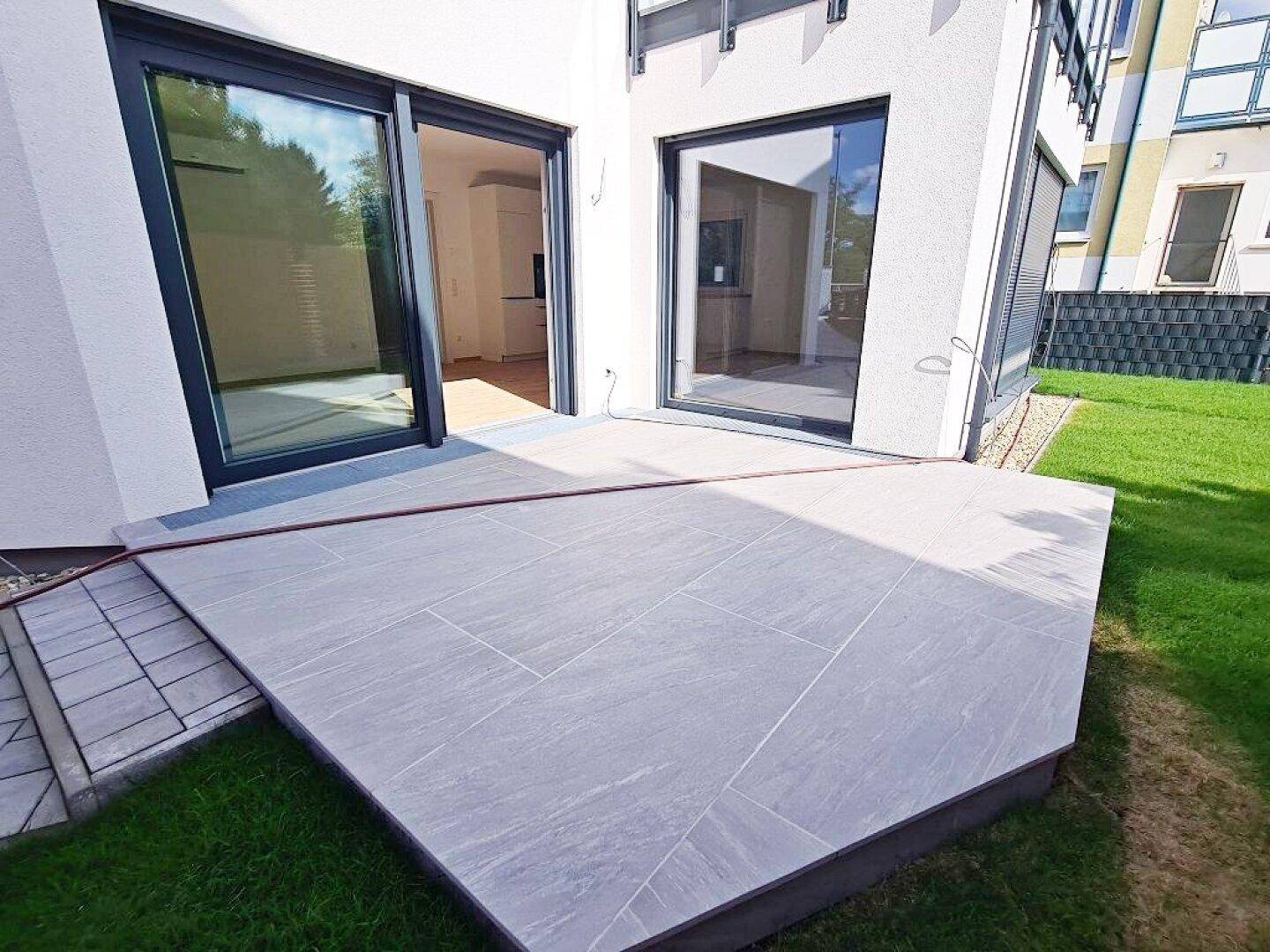 Moderne geflieste Terrasse mit Zugang zum Garten und großen Schiebetüren ins Haus.