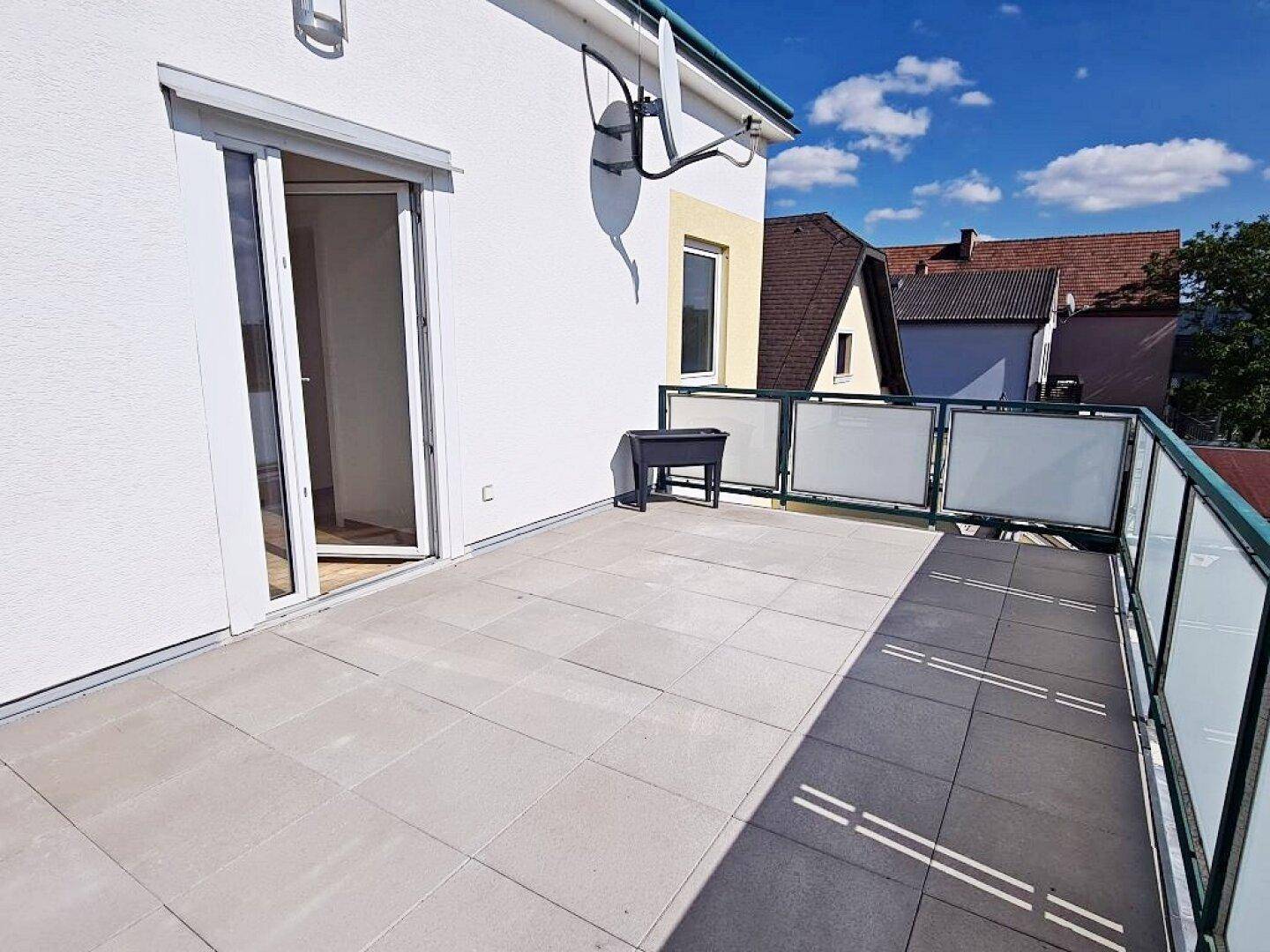 Große Terrasse mit Fliesenboden, Glasbrüstung und Satellitenschüssel an der Fassade.