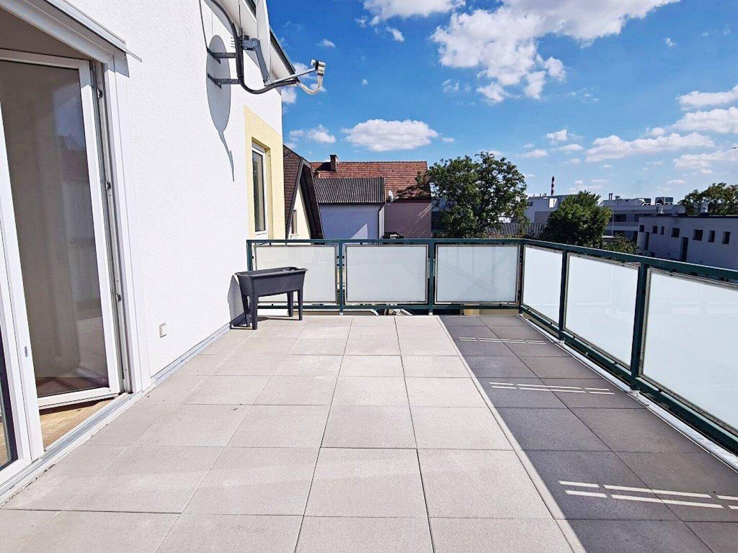 Weitläufige Terrasse mit Fliesenboden und Glasbrüstung, bietet einen weiten Blick in die Umgebung.