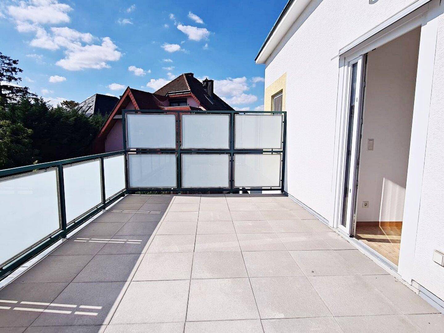 Sonnige Terrasse mit Fliesenboden und Glasbrüstung, mit direktem Zugang zum Innenbereich.
