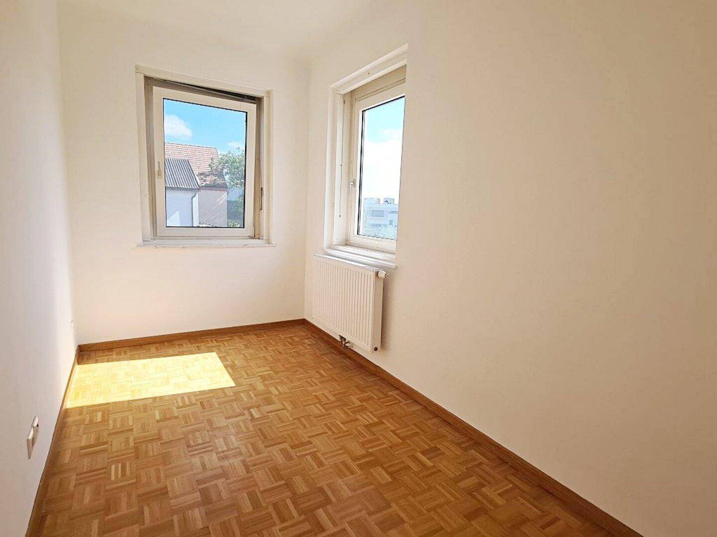 Kleineres, helles Zimmer mit Parkettboden und zwei Fenstern, ideal als Kinder- oder Arbeitszimmer.