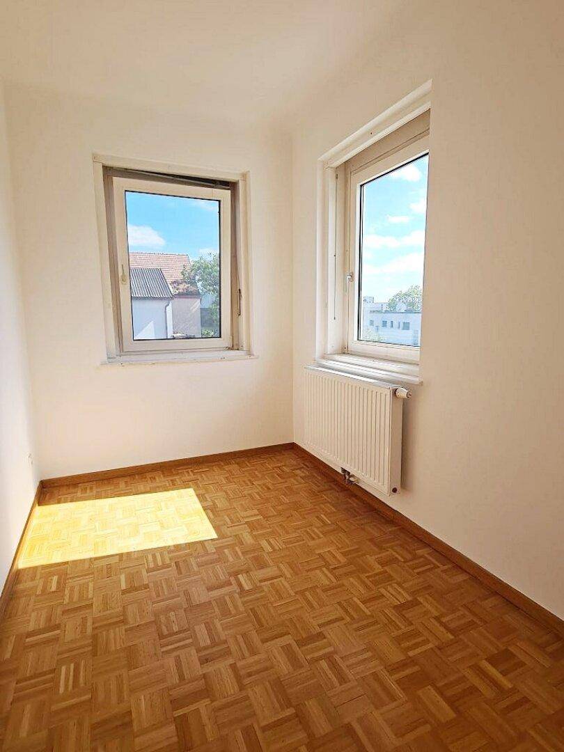 Helles Zimmer mit Parkettboden und zwei Fenstern, die für eine angenehme Belichtung sorgen.