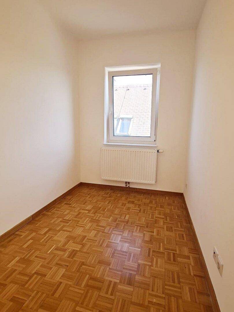 Kleines, helles Zimmer mit Parkettboden und einem Fenster, das viel Tageslicht bietet.