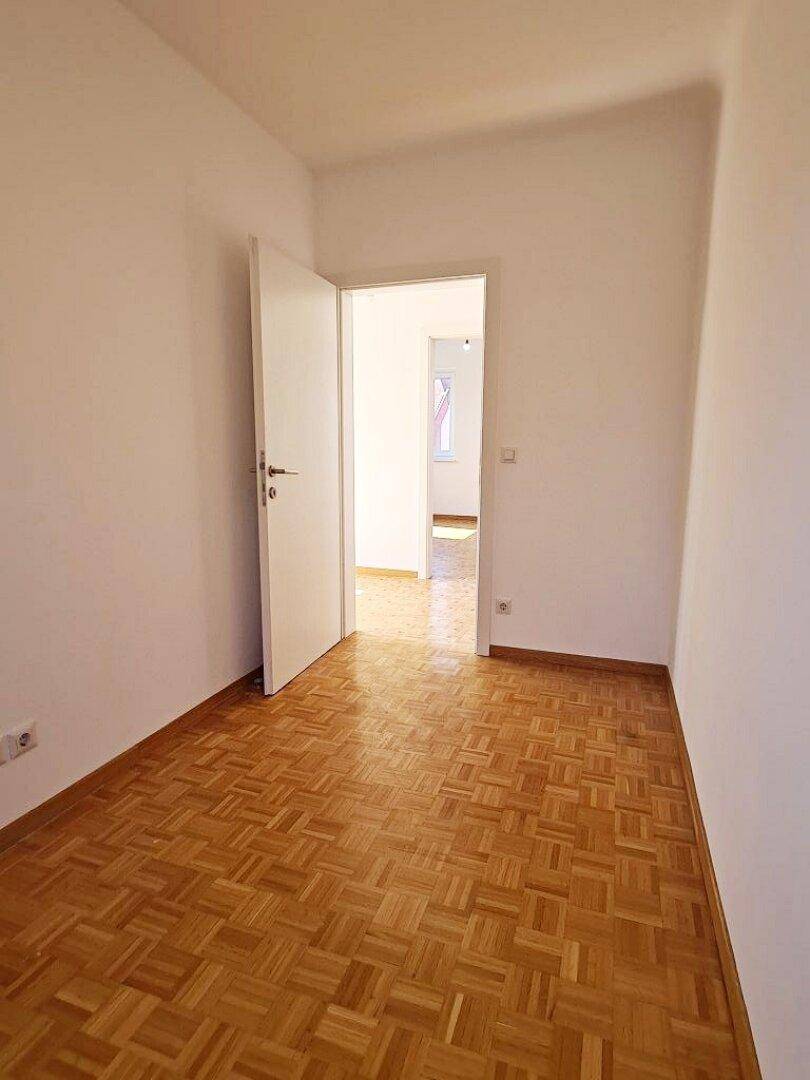 Leeres Zimmer mit Parkettboden und offenem Durchgang, bereit für individuelle Gestaltung.