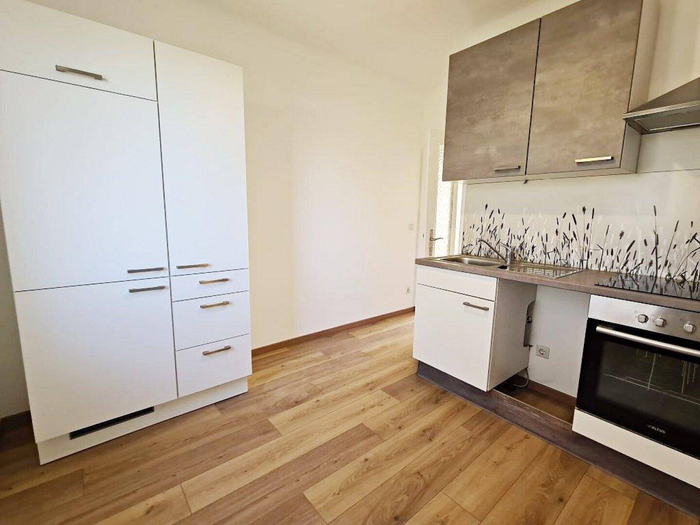 Kleine Küche mit Laminatboden und einem hohen Schrank, bietet Stauraum und Arbeitsfläche.