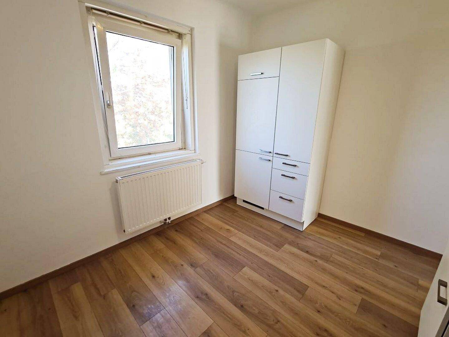 Helles Zimmer mit Holzfußboden und einem weißen Kleiderschrank, ideal als Schlaf- oder Gästezimmer.