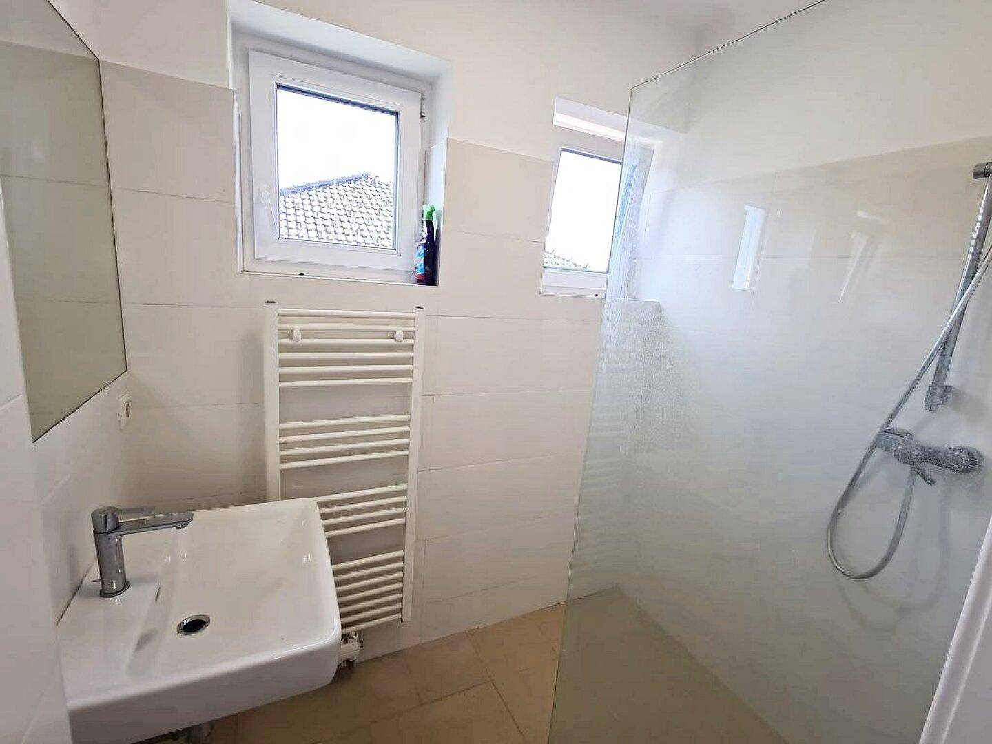 Modernes Badezimmer mit Dusche, Waschbecken, Fenster und beheiztem Handtuchhalter.