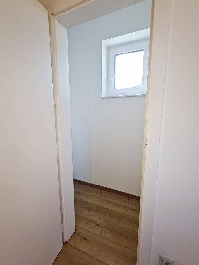 Kleiner, heller Raum mit Fenster und Holzfußboden, nutzbar als Abstellraum oder begehbarer Kleiderschrank.