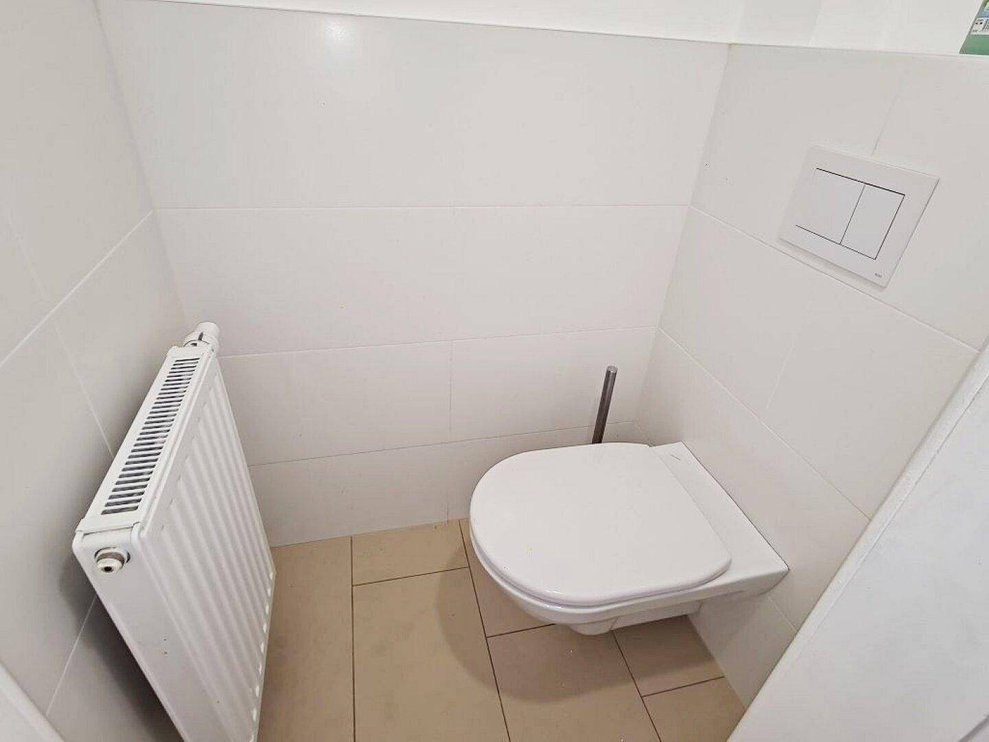 Separates WC mit wandhängender Toilette und Heizkörper, ausgestattet mit hellen Fliesen.