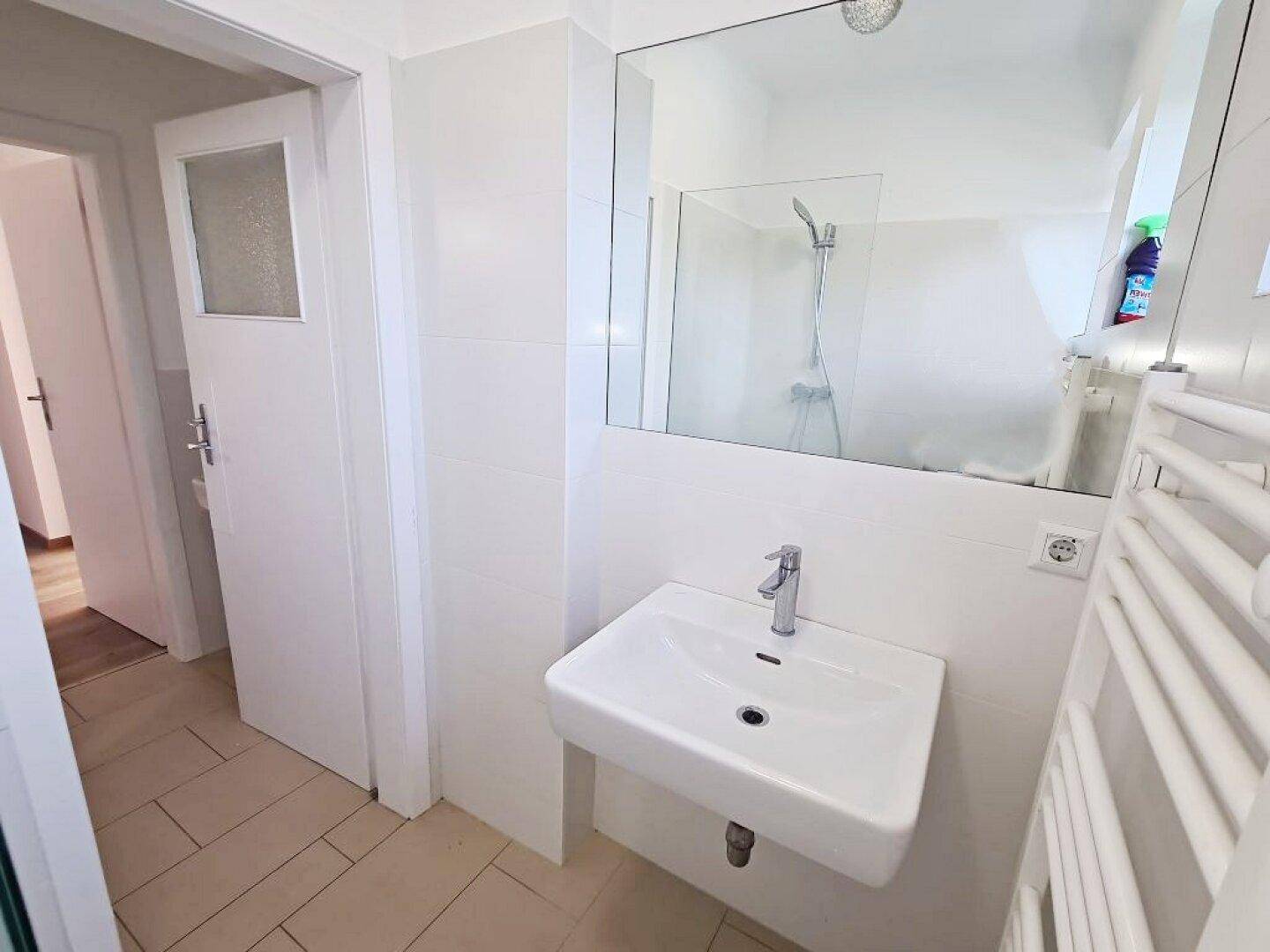 Badezimmer mit modernem Waschbecken, großem Spiegel und Zugang zu weiteren Räumen.