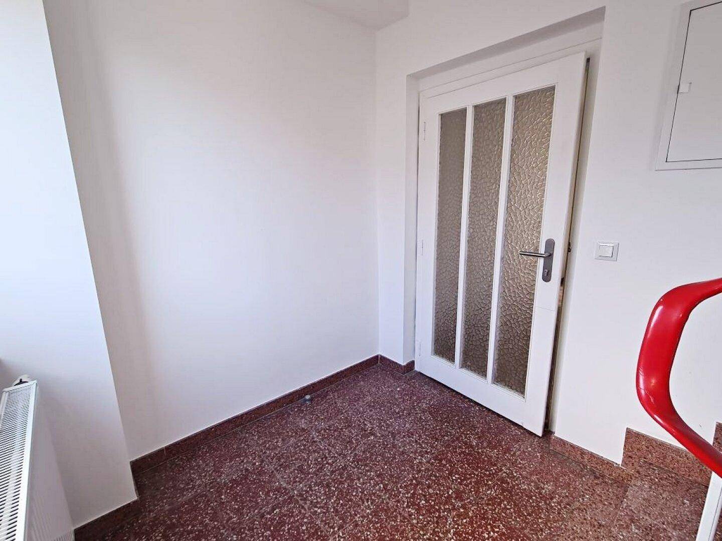Eingangsbereich mit Terrazzoboden und einer Tür mit Glaseinsätzen, die zum Treppenhaus führt.