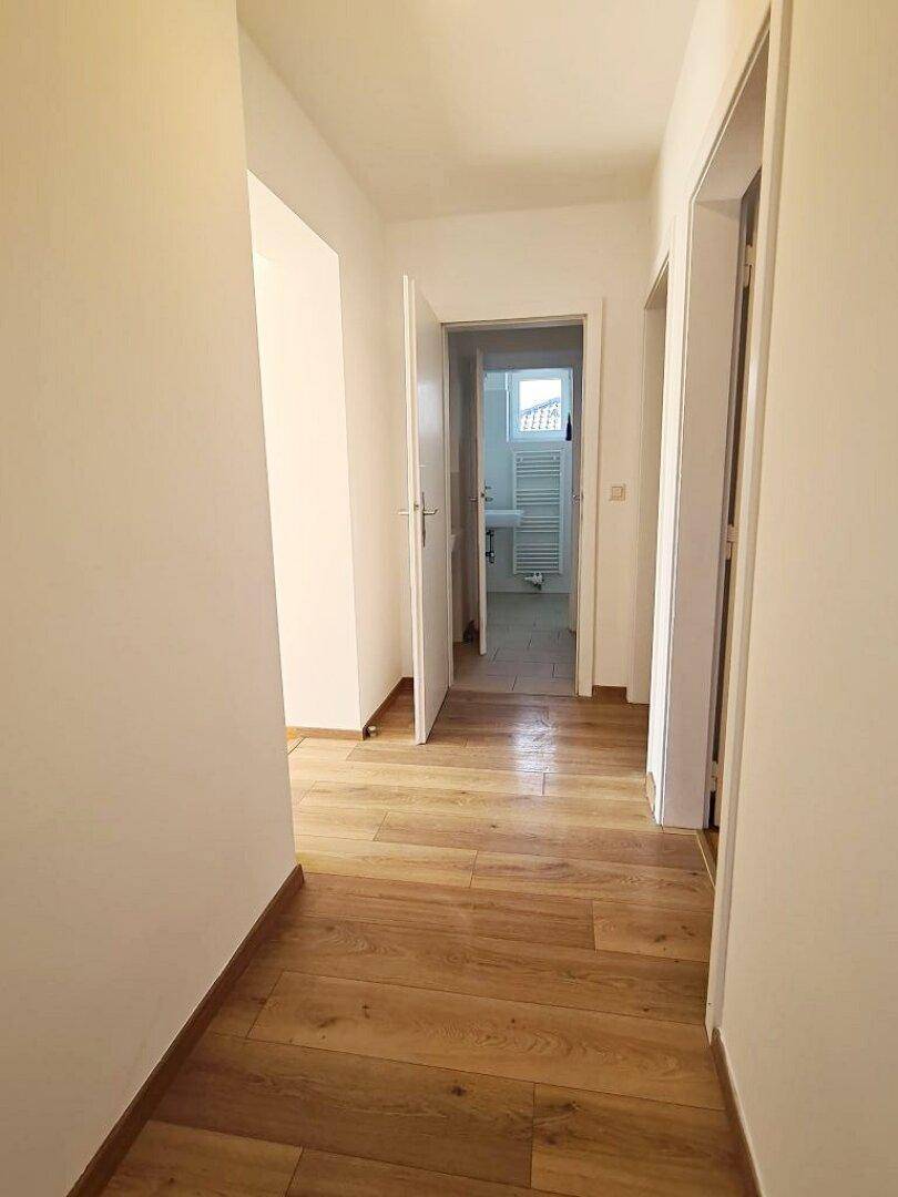 Langer Flur mit Holzfußboden, der verschiedene Räume verbindet und einen Blick ins Badezimmer bietet.
