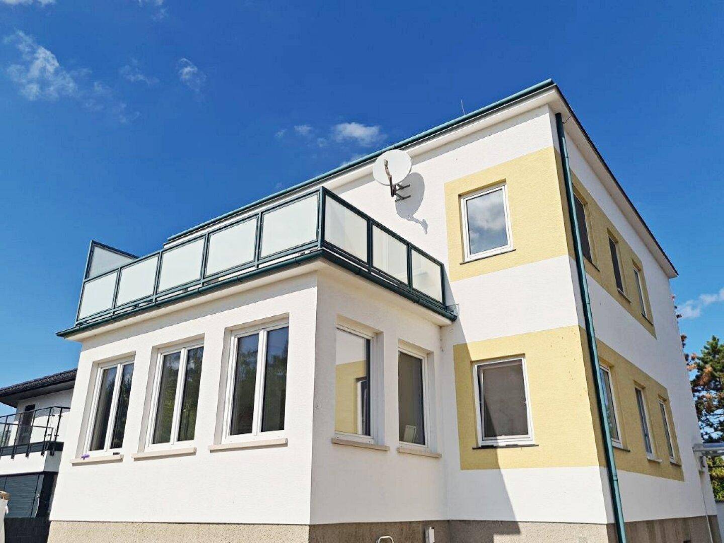 Außenansicht des Gebäudes mit gelb-weißer Fassade und einer Terrasse im Obergeschoss.