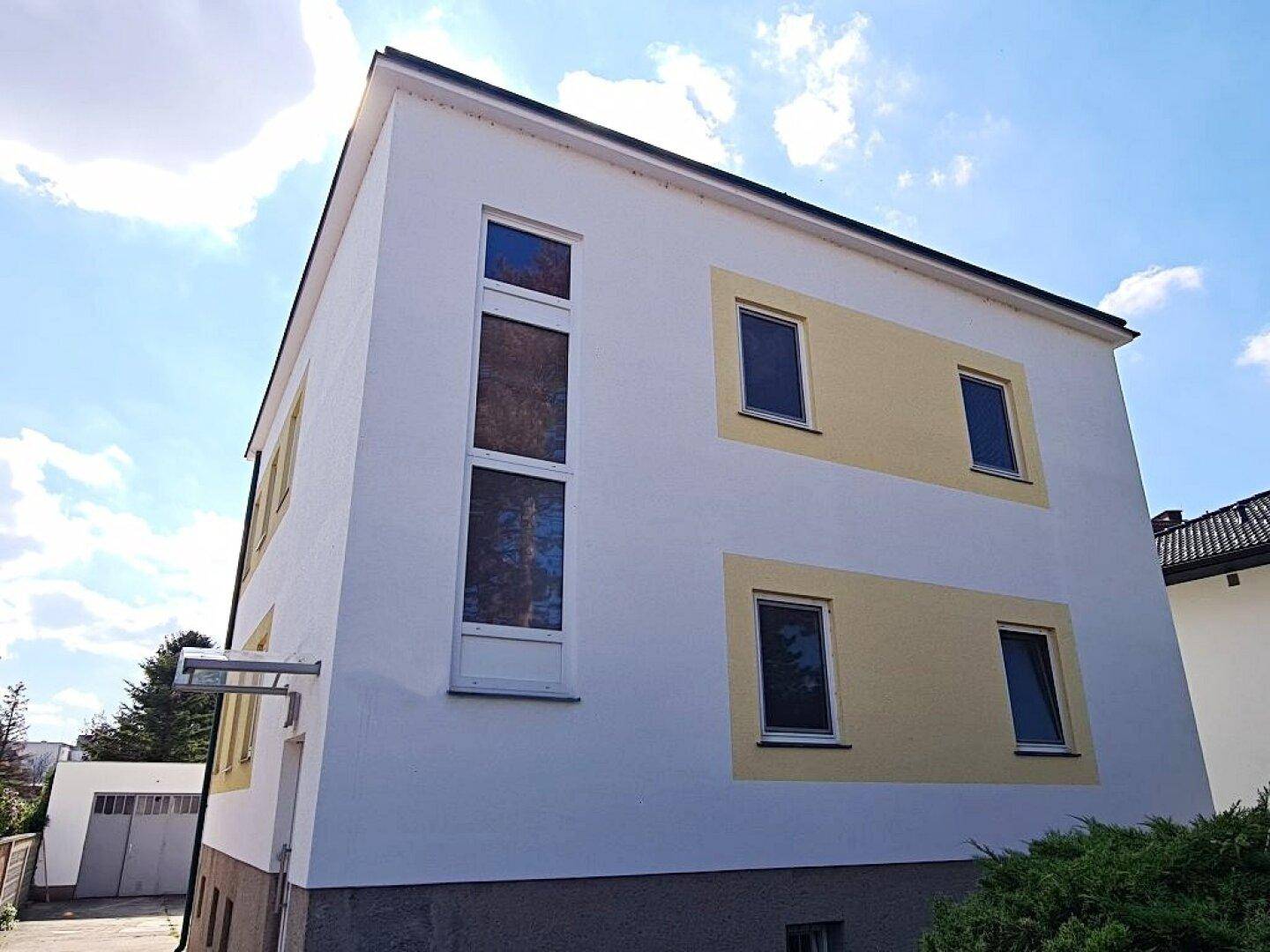 Seitenansicht eines gepflegten Gebäudes mit gelben Akzenten und modernen Fenstern unter blauem Himmel.
